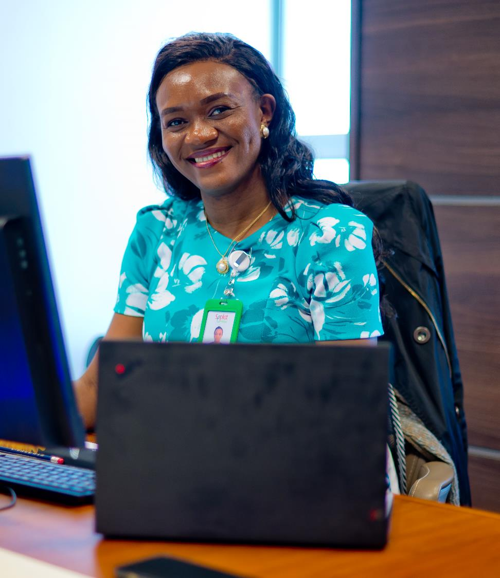 Woman in a teal floral top wearing a Seplat ID badge, smiling at a desk with a laptop.