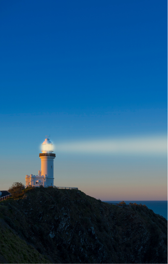 Lighthouse beaming a bright light across the coastline at dusk.